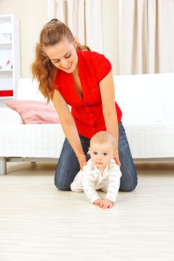 Smiling mother helping cheerful baby learn to creep clipart