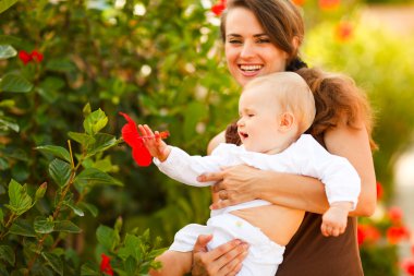 Happy mother showing flower to her baby on street clipart