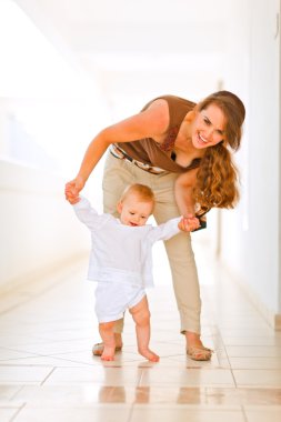 Happy mom helping baby to walk clipart