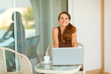 Happy young woman sitting on terrace with cup of coffee and lapt clipart