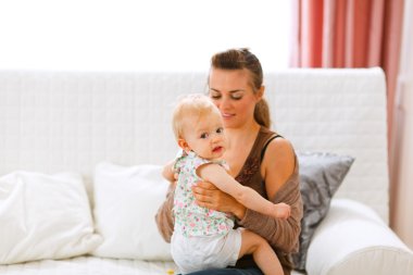 Funny baby sitting on mamas knees and looking back clipart