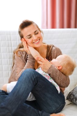 Young woman enjoying of being mother put baby's hand to her chee clipart