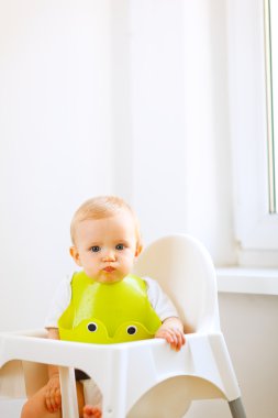 Portrait of lovely eat smeared baby sitting in baby chair clipart