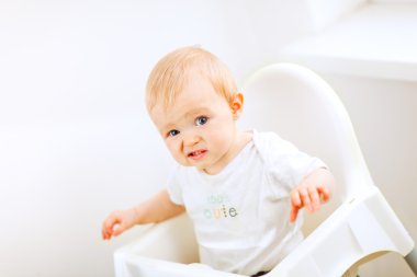 Adorable baby sitting in baby chair and making funny face clipart