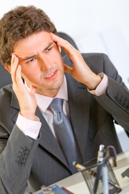 Portrait of stressed modern businessman sitting at office desk clipart