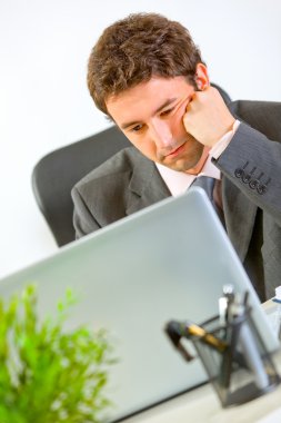 Bored modern businessman working on laptop at office clipart