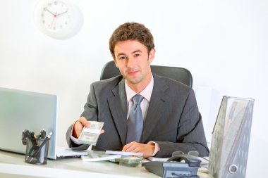 Modern businessman sitting at office desk and giving money packs clipart