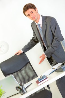 Modern businessman offering to seat at office desk clipart