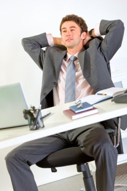 Pleased modern businessman relaxing on office armchair clipart