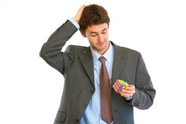 Confused businessman holding Rubik's cube in hand clipart