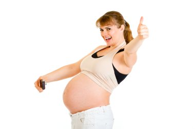 Pregnant woman photographing her belly and showing thumbs up gesture