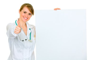 Smiling medical female doctor holding blank billboard and showing thumbs up clipart