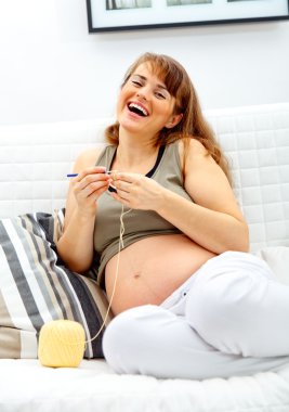 Laughing beautiful pregnant woman knitting for her baby. clipart