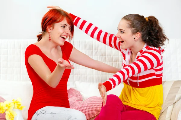 Two happy girlfriends sitting on sofa and cheerfully embracing — Stock Photo, Image