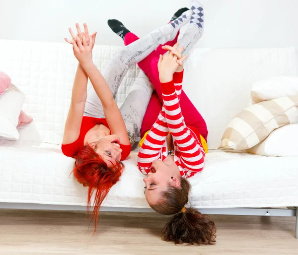 Namoradas engraçadas no humor brincalhão deitado no sofá com as pernas levantadas — Fotografia de Stock