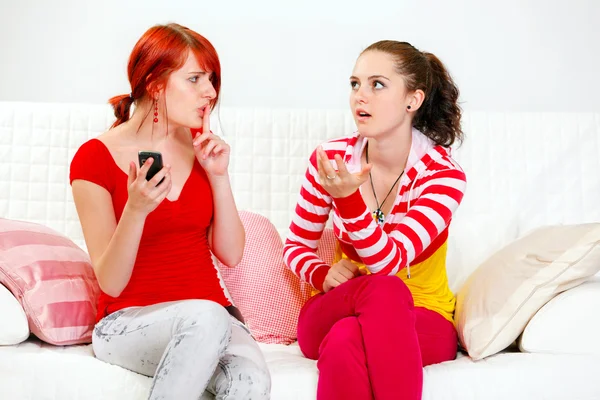 Girl with mobile showing silence gesture her indignant girlfriend — Stock Photo, Image