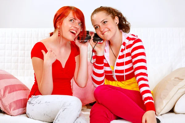 Sitting on sofa two girlfriends holding headphones and listening music — Stock Photo, Image