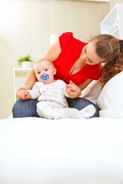 Joven madre acostada en el sofá y jugando con el bebé — Foto de Stock