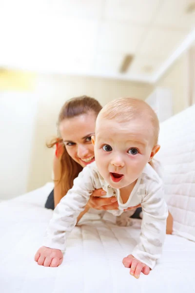 Gelukkig moeder en interesse baby spelen op divan — Stockfoto