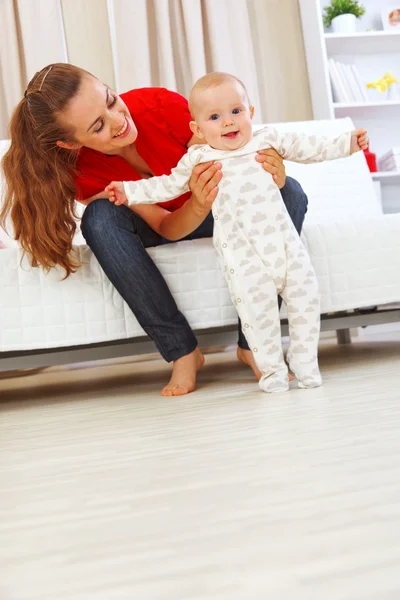 Sonriente madre ayudando a bebé alegre aprender a caminar —  Fotos de Stock