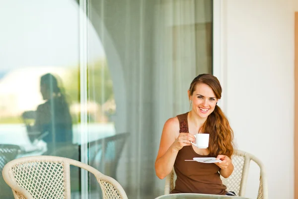 Χαμογελώντας νεαρή γυναίκα που κάθεται στην βεράντα και πίνοντας καφέ — Φωτογραφία Αρχείου
