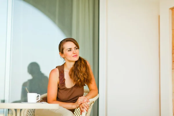 Thoughtful young female sitting on terrace with cup of tea and — Stock Photo, Image