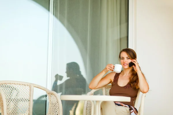 Concerned young female sitting on terrace with cup of coffee and — Stock Photo, Image