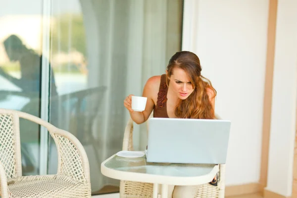 Jovem curiosa com xícara de chá olhando no laptop — Fotografia de Stock