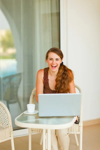Mujer joven sonriente sentada en la terraza con una taza de café y la —  Fotos de Stock