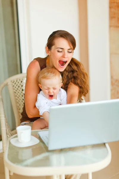 Junge Mutter und Baby gähnen beim Arbeiten am Laptop — Stockfoto