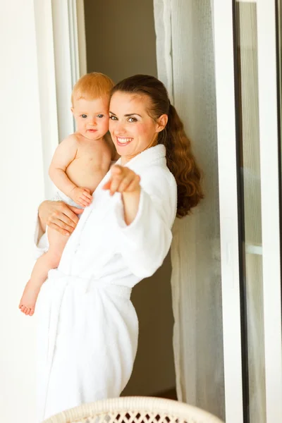 Retrato de mamá joven en albornoz con el bebé en la mano apuntando en la cámara — Foto de Stock