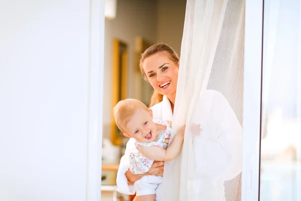 Portret van lachende moeder in badjas met baby uitkijken fro — Stockfoto