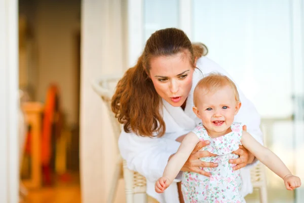 Young mother in bathrobe telling something to her adorable baby — Stock Photo, Image