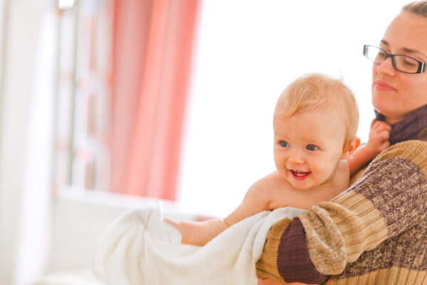 Cheerful baby on mamas arms looking in corner
