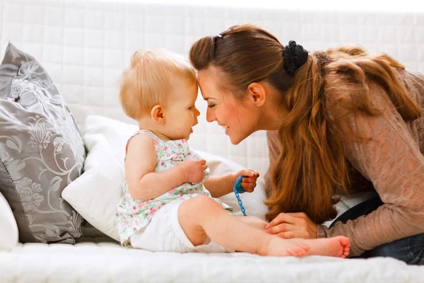 Cute baby with soother and young mom playing on divan — Stock Photo, Image