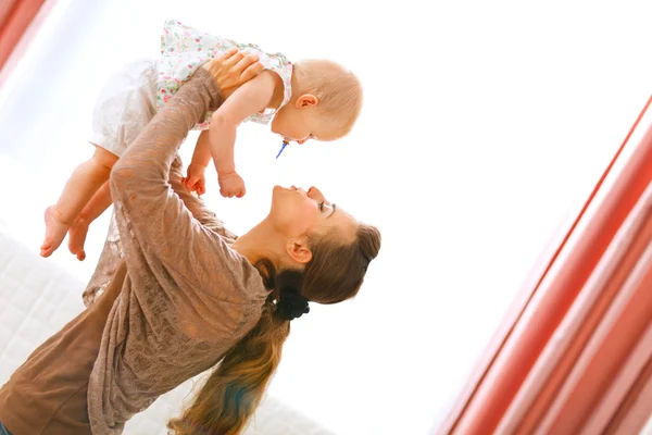 Jovem mãe brincando com o bebê, levantando-a — Fotografia de Stock