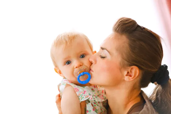 Молодая мама целует ребенка с успокаивающим — стоковое фото