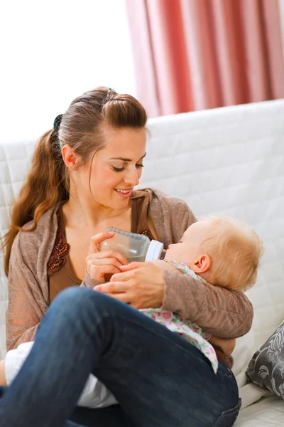 Jovem mãe sentada no sofá e alimentando seu bebê — Fotografia de Stock