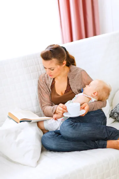 Giovane mamma che riposa mentre il bambino dorme prendendo il tè e leggendo boo — Foto Stock