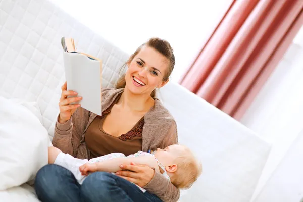 Smiling young mother resting while baby sleep by reading book — Stock Photo, Image