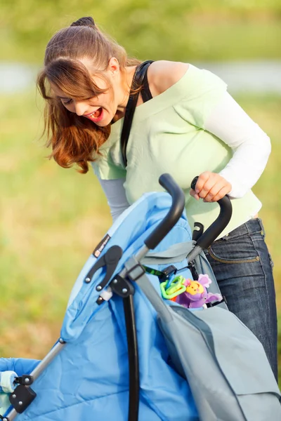 Laughing mother looking in stroller while walking in park — Stock Photo, Image