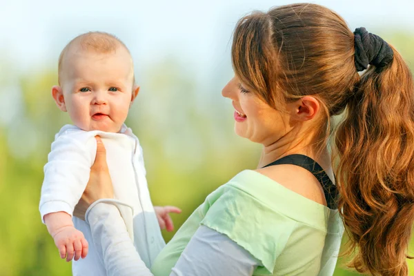 Lachende moeder bedrijf verbaasd baby in handen over zomerdag — Stockfoto