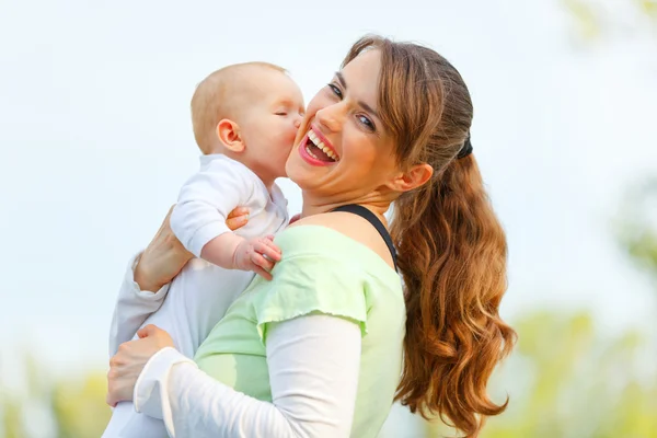 Lachen moeder haar baby knuffelen in handen buitenshuis — Stockfoto