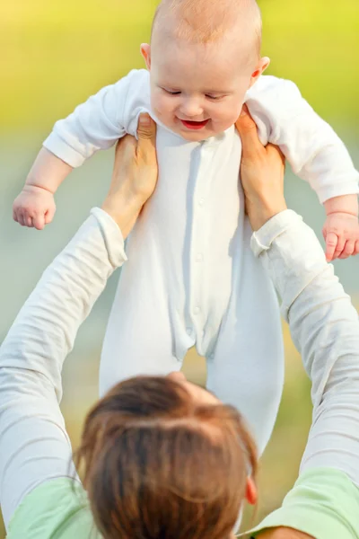 Mor anläggning skrattande bebis i händer utomhus på sommardag. närbild. — Stockfoto