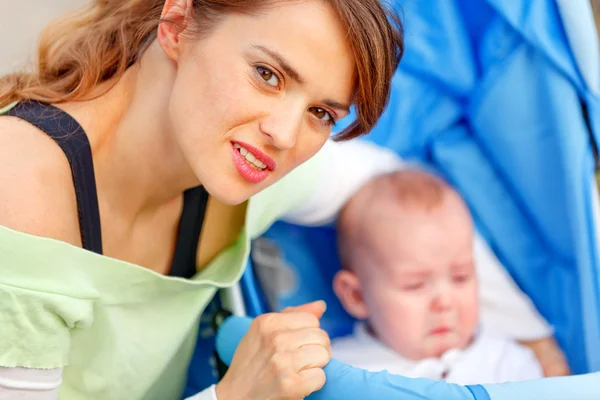 思いやりのある母親が抱いて泣いている赤ちゃんのベビーカーに座っています。 — ストック写真
