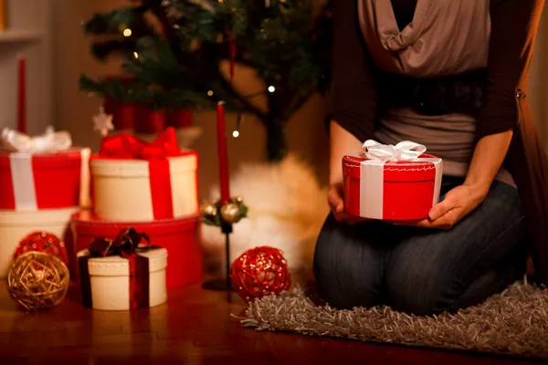 Крупный план на подарочной коробке в руке женщины, сидящей возле елки — стоковое фото