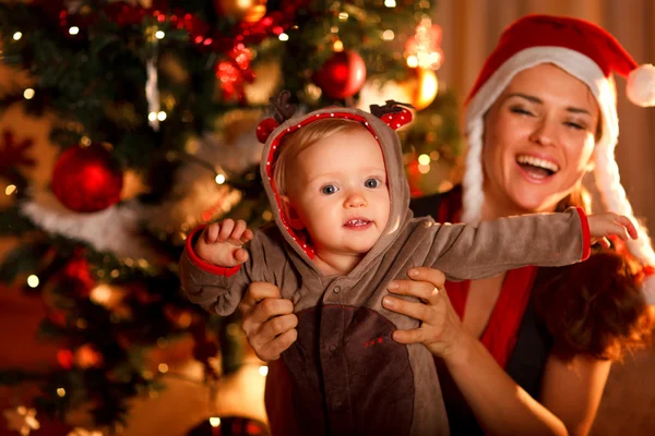 Lycklig mor leker med barnet nära julgran — Stockfoto