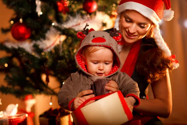 Mladá matka pomáhá zájem dítěte otevřené krabičce na Vánoce — Stock fotografie