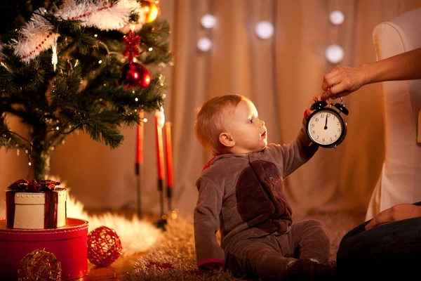 Precioso bebé cerca del árbol de Navidad sosteniendo con madre despertador —  Fotos de Stock