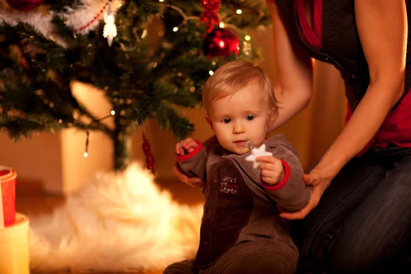 Веселый малыш сидит с мамой возле елки и смотрит на — стоковое фото